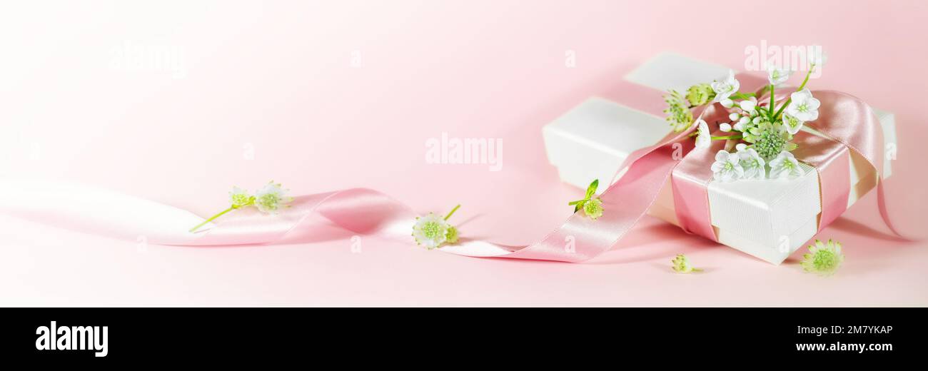 Cadeau romantique d'amour avec ruban et fleurs blanches sur fond de pêche rose en format panoramique pour la Saint Valentin, la fête des mères, l'anniversaire ou le mariage, Banque D'Images