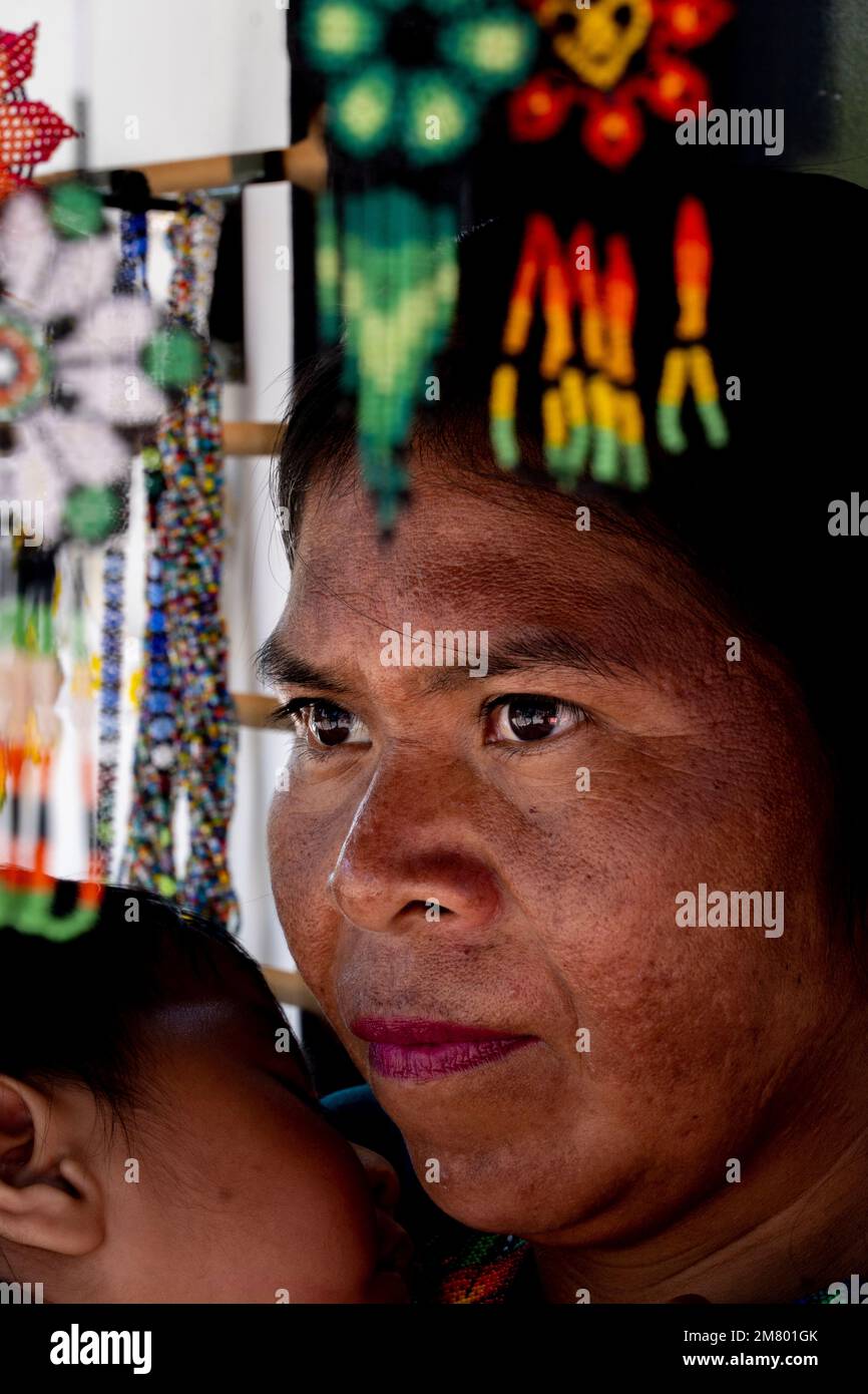 femme artisanale traditionnelle portant sa fille, entourée de son artisanat chaquira très coloré Banque D'Images