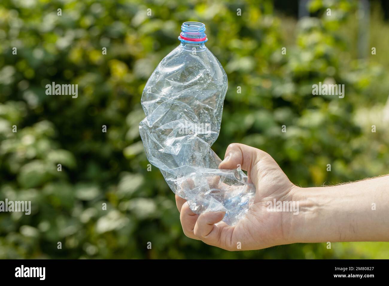 Main tenant une bouteille en plastique vide froissés dans le parc Banque D'Images