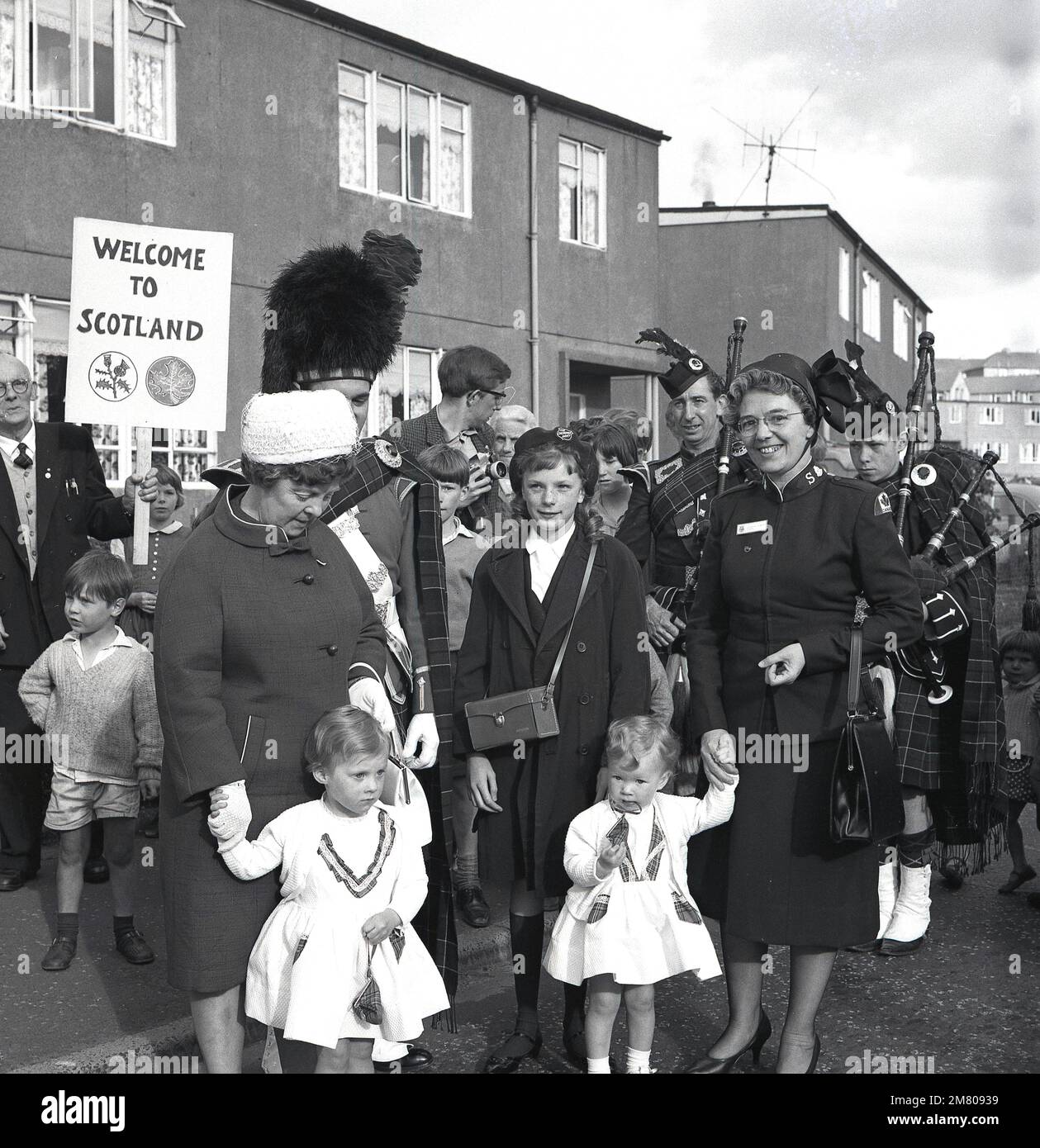 1960s, le groupe historique de bagpipe joue dans la rue, comme une dame de l'Armée du Salut au Canada paie un vistor au twon/village, Fife, Écosse, Royaume-Uni. Banque D'Images