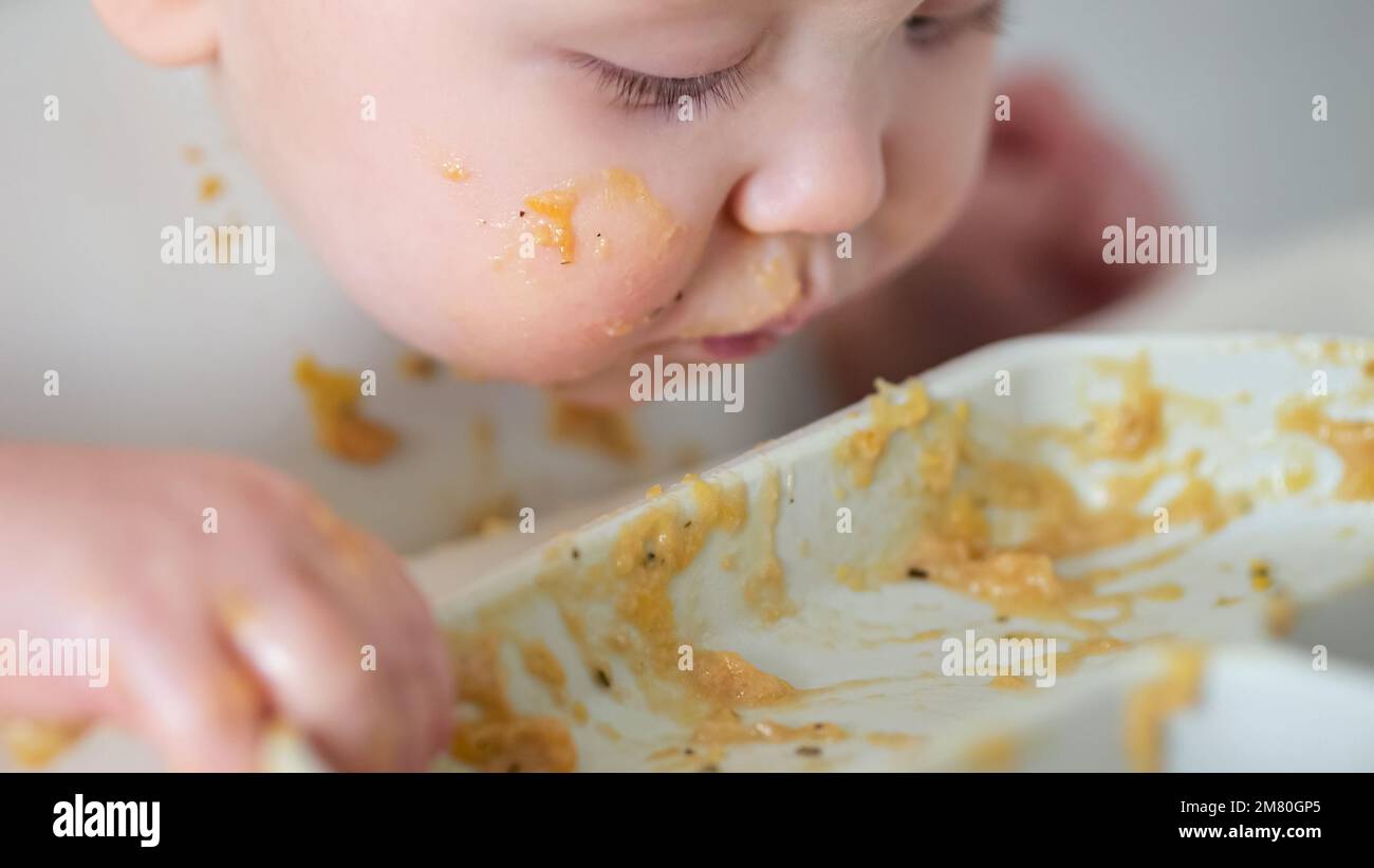 Bébé fille saisit les restes de nourriture et mange avec enthousiasme Banque D'Images