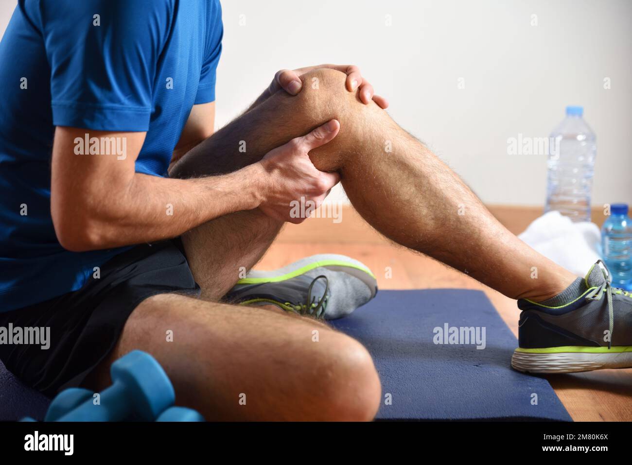 Détail de l'homme faisant du sport avec des douleurs au genou se tenant avec sa main assise sur un tapis. Vue latérale. Banque D'Images