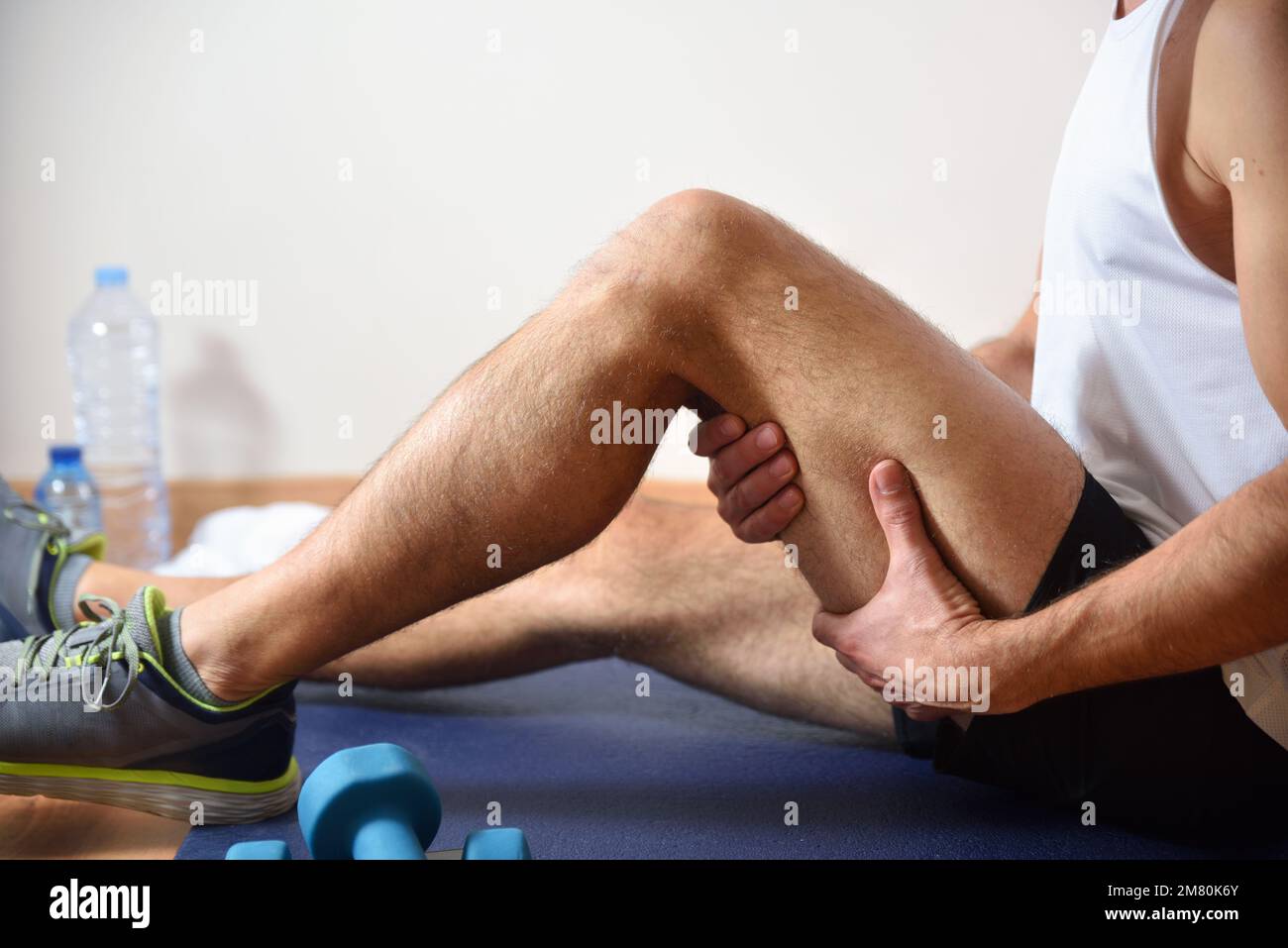 Détail de l'homme faisant du sport avec des hamstrings douleur se tenant avec sa main assise sur un tapis. Vue latérale Banque D'Images