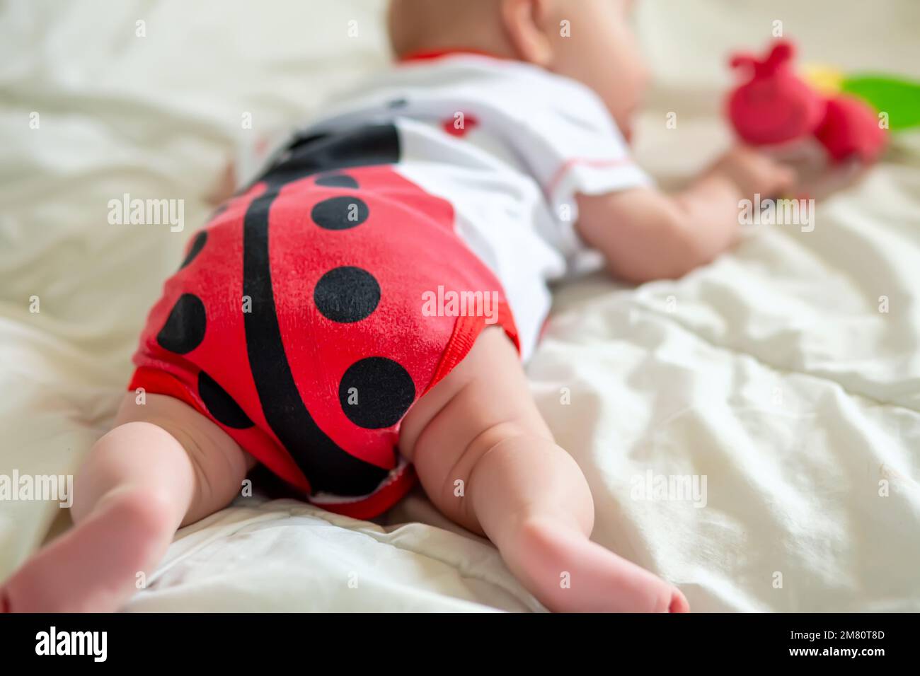 Un enfant de 2 mois rampant sur le lit au premier jouet. Stimulation de l'rampement. Enseigner à un enfant jusqu'à six mois Banque D'Images