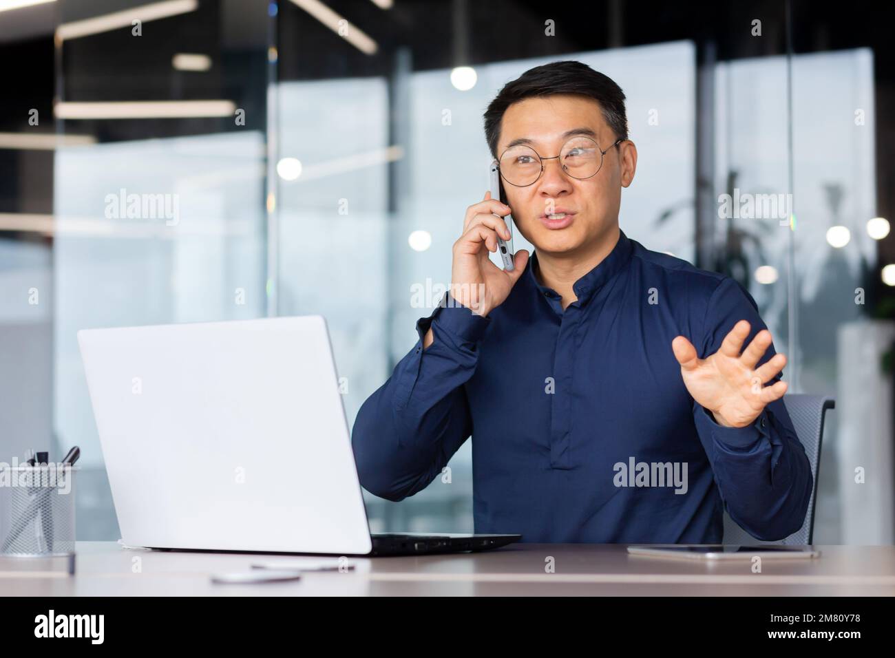 Jeune homme, homme d'affaires asiatique, étudiant, parlant au téléphone avec des clients et des partenaires. Assis dans le bureau à la table, travaillant sur l'ordinateur portable. Banque D'Images