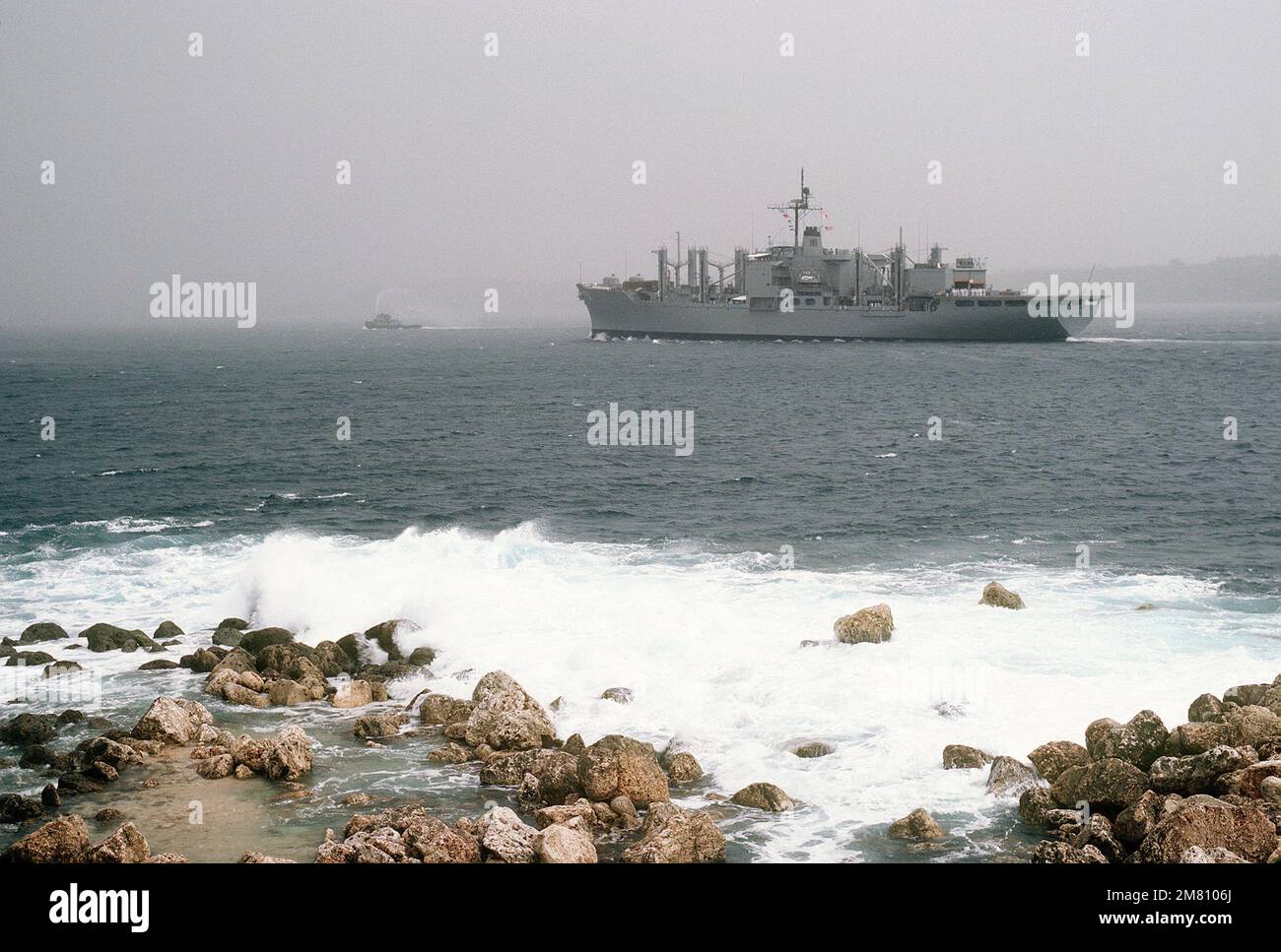 Vue sur le quartier portuaire des magasins de combat navire USS NIAGARA FALLS (AFS 3) et un grand remorqueur de port entrant dans le port d'Apra. Base: Orote point État: Guam (GU) pays: Îles Mariannes du Nord (MNP) Banque D'Images