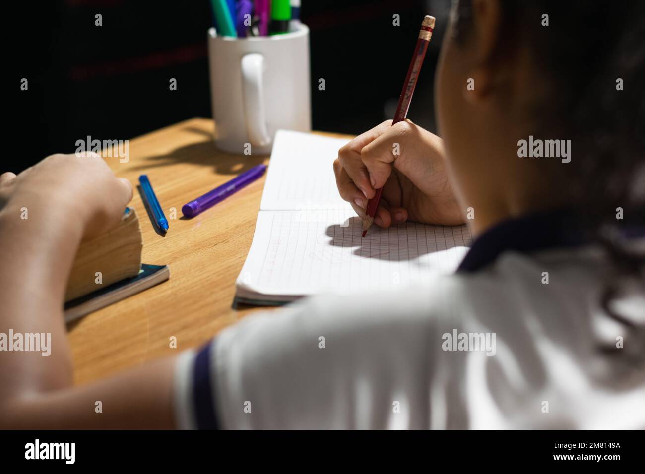 vue détaillée des mains d'une petite fille latine qui s'affiche sur son carnet au-dessus d'un bureau en bois. faire ses devoirs. Banque D'Images