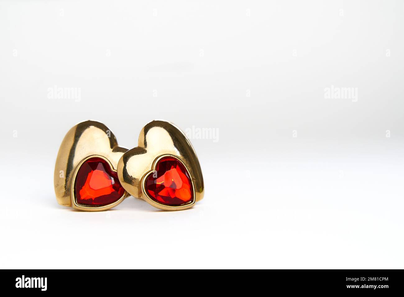 Concept d'amour de la Saint-Valentin. Deux boucles d'oreilles dorées en forme de coeur avec des rubis sur fond blanc Banque D'Images