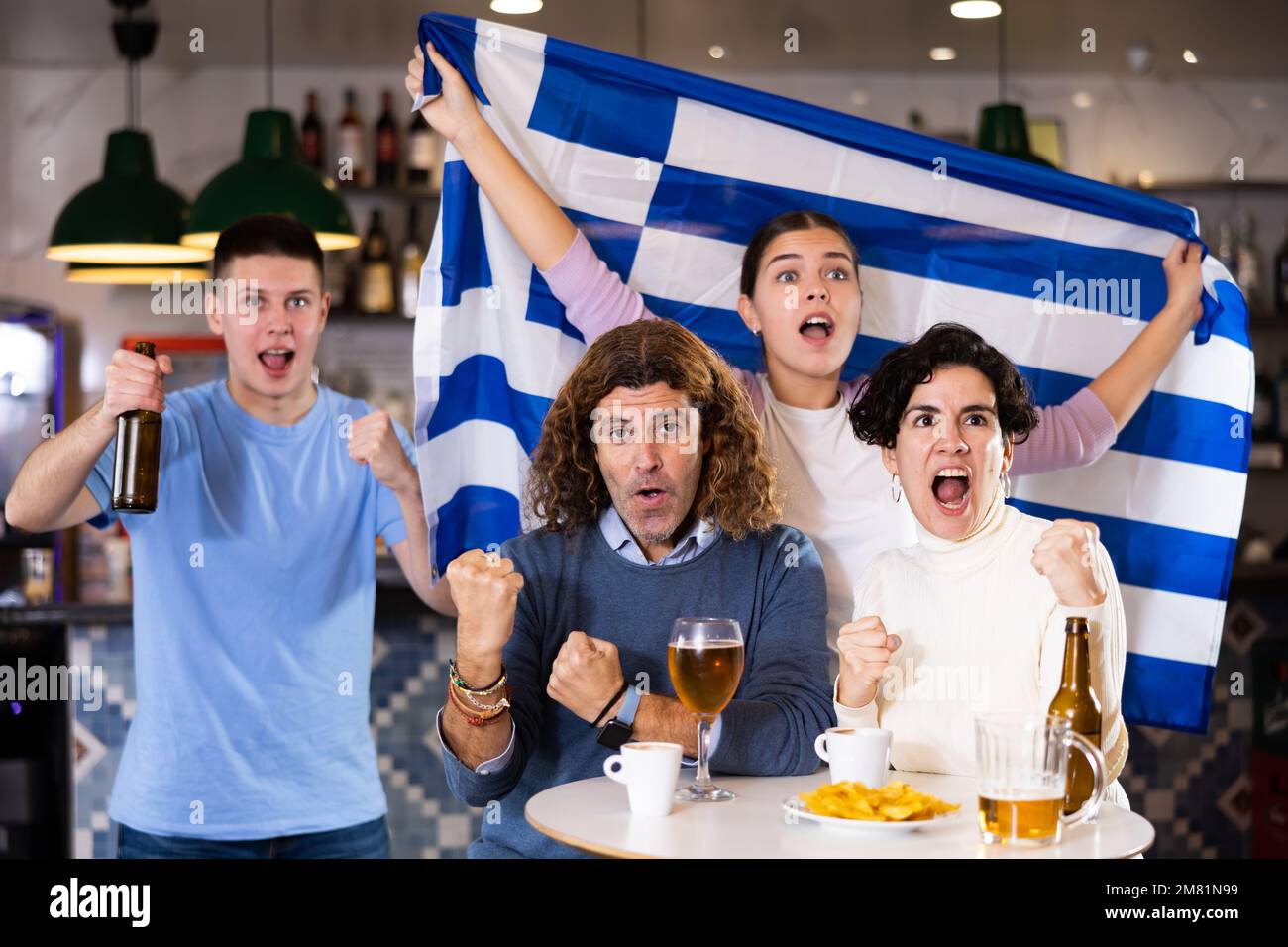 Groupe d'amis émotifs supporters applaudissent pour l'équipe préférée avec le drapeau de la Grèce tout en regardant le match à la télévision dans le pub Banque D'Images