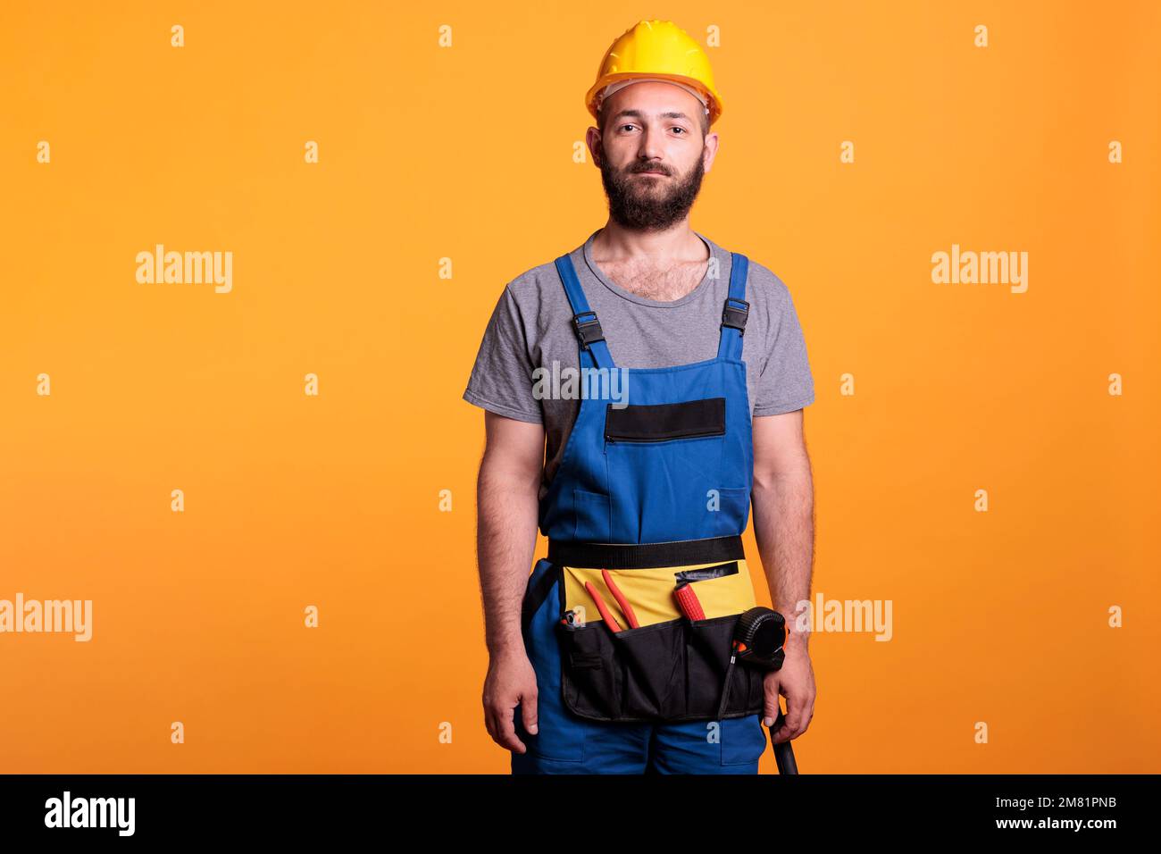 Travailleur de construction confiant portant un uniforme et un casque de rénovation, posant sur la caméra en studio. Réparateur professionnel se préparant à travailler sur un projet de rénovation, expert artisan. Banque D'Images
