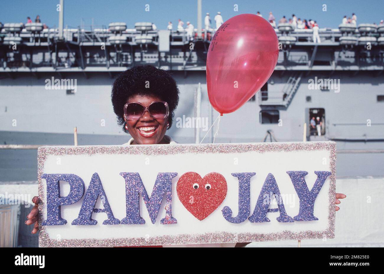 Pat Thomas, épouse de Fireman (FN) Jonathan Thomas, tient un panneau accueillant son mari de retour au port d'attache après 11 mois en mer à bord du navire USS NEW JERSEY (BB 62). Une partie du navire d'assaut amphibie USS PELIU (LHA 5) peut être vue en arrière-plan. Base: Naval Air Station, long Beach État: Californie (CA) pays: Etats-Unis d'Amérique (USA) Banque D'Images