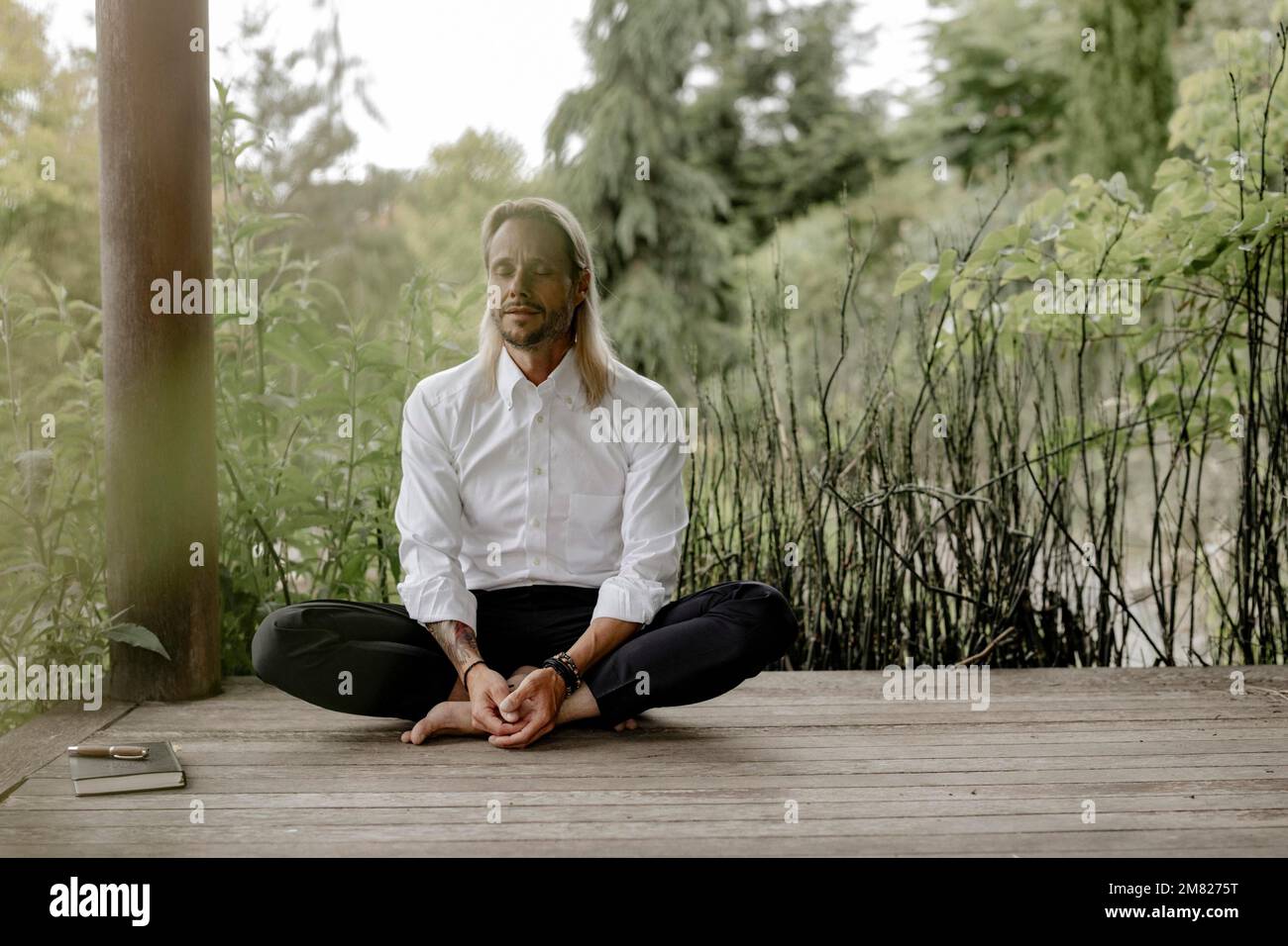 Homme d'affaires en chemise blanche est assis sur une jetée en bois et écrit dans un livre Banque D'Images