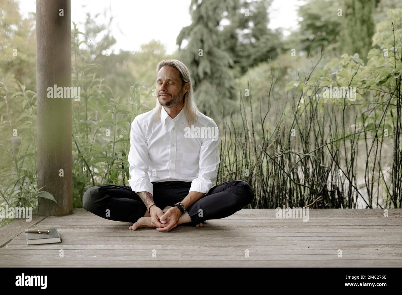 Homme d'affaires en chemise blanche est assis sur une jetée en bois et écrit dans un livre Banque D'Images