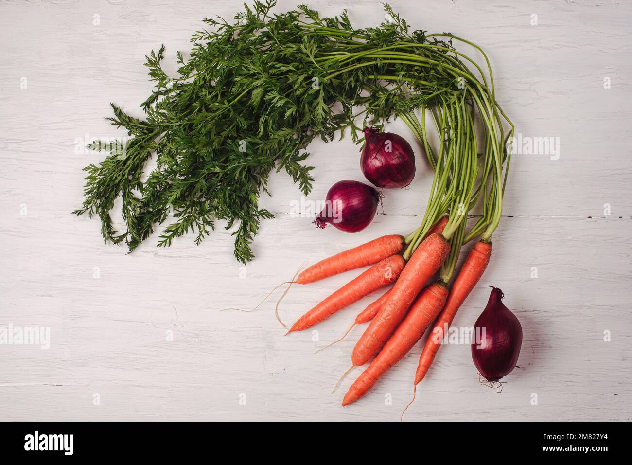 Carotte avec des légumes verts et oignon sur une table en bois blanc. Alimentation végétalienne saine, concept de récolte. Vue de dessus, plan d'agencement. Banque D'Images