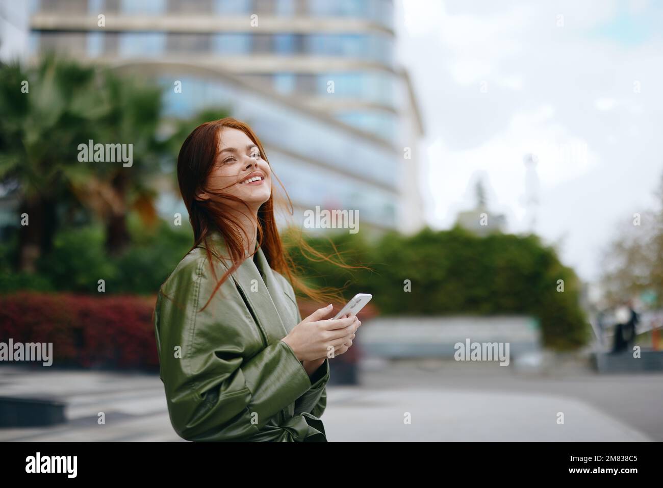 Femme d'affaires de mode avec téléphone à la main dans les vêtements tendance sourire marchant autour de la ville près des bâtiments de bureau, travail en ligne technologie de shopping Banque D'Images