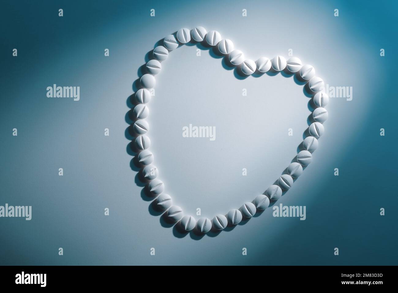 Forme de coeur des pilules blanches sur fond blanc clair en lumière bleue dure avec ombre, vue de dessus Banque D'Images