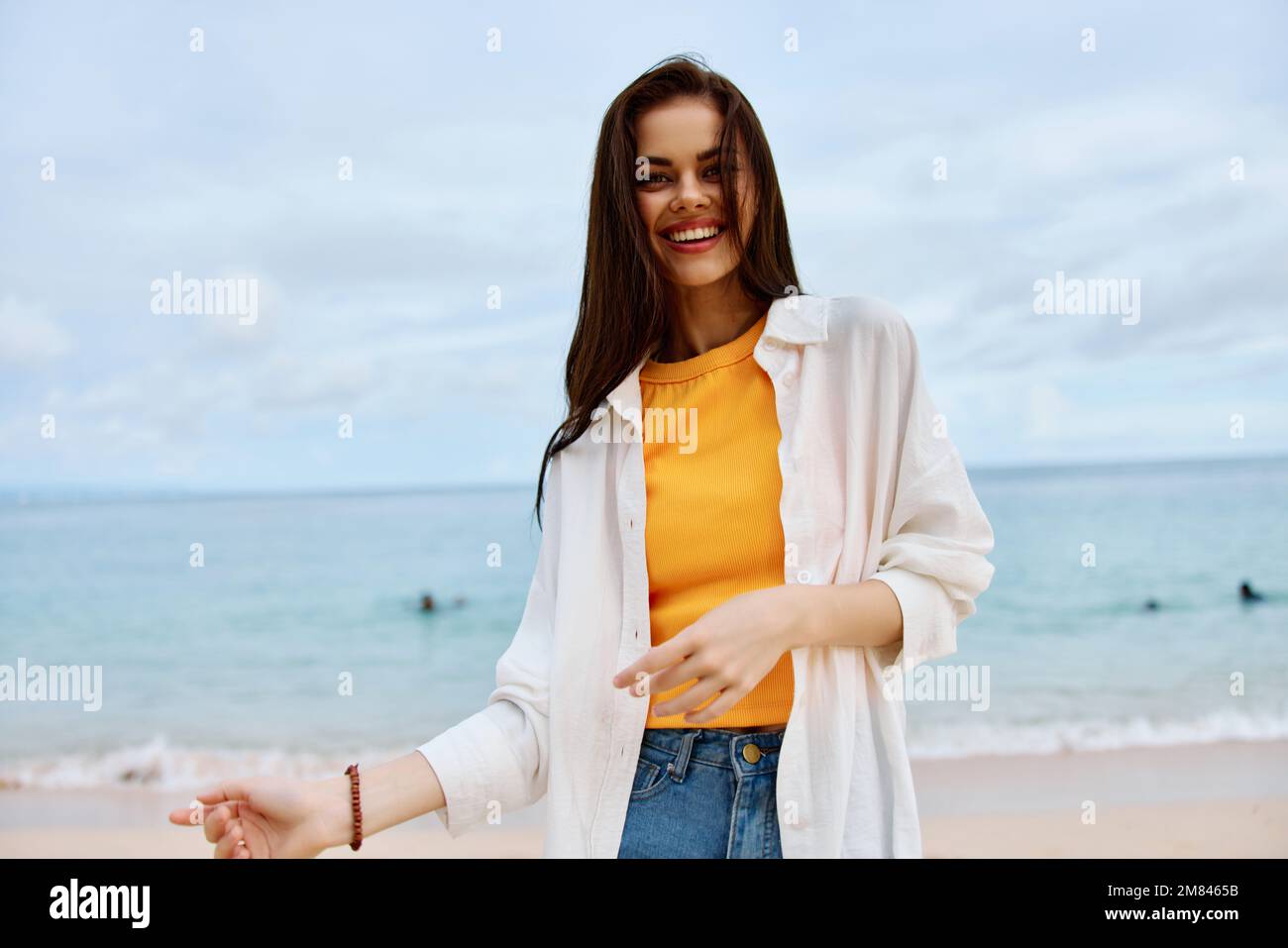 Portrait d'une femme heureuse souriant avec des dents avec de longs cheveux brunette marche le long de la plage dans un réservoir jaune short en denim et une chemise blanche par le Banque D'Images