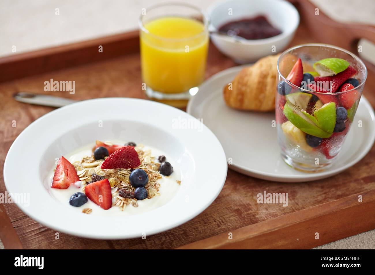 Nutritif et délicieux. Gros plan sur un plateau petit déjeuner avec jus de fruits, salade de fruits, croissant et muesli. Banque D'Images