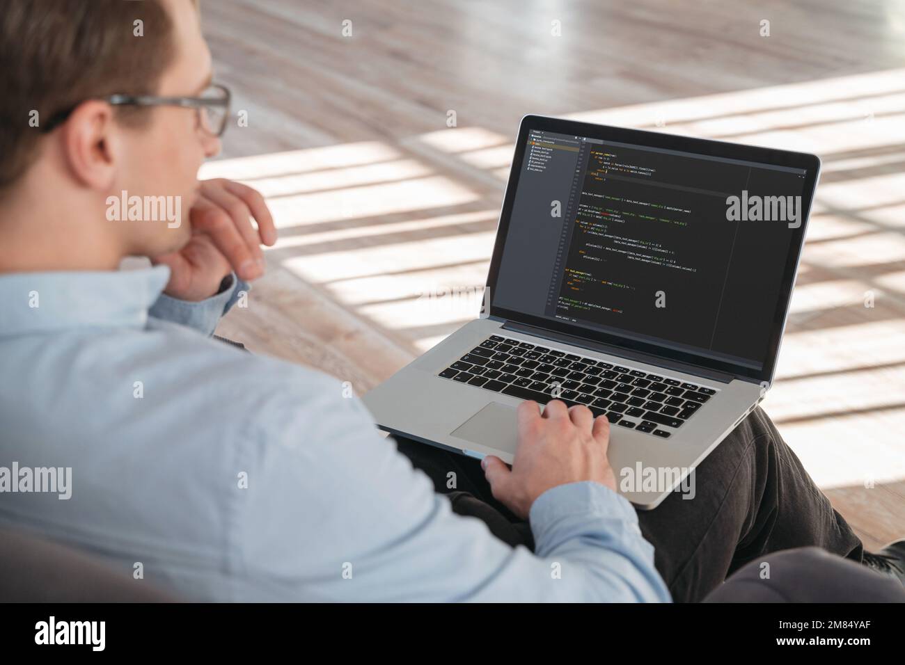 Gros plan d'un codeur assis avec un ordinateur portable à genoux, travaillant en ligne sur un nouveau PRODUIT INFORMATIQUE. Banque D'Images