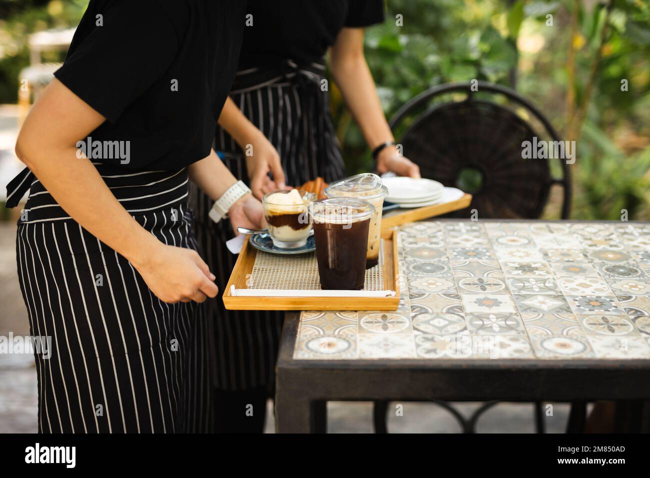 Serveuse avec tablier servant du café glacé au client au café. Banque D'Images