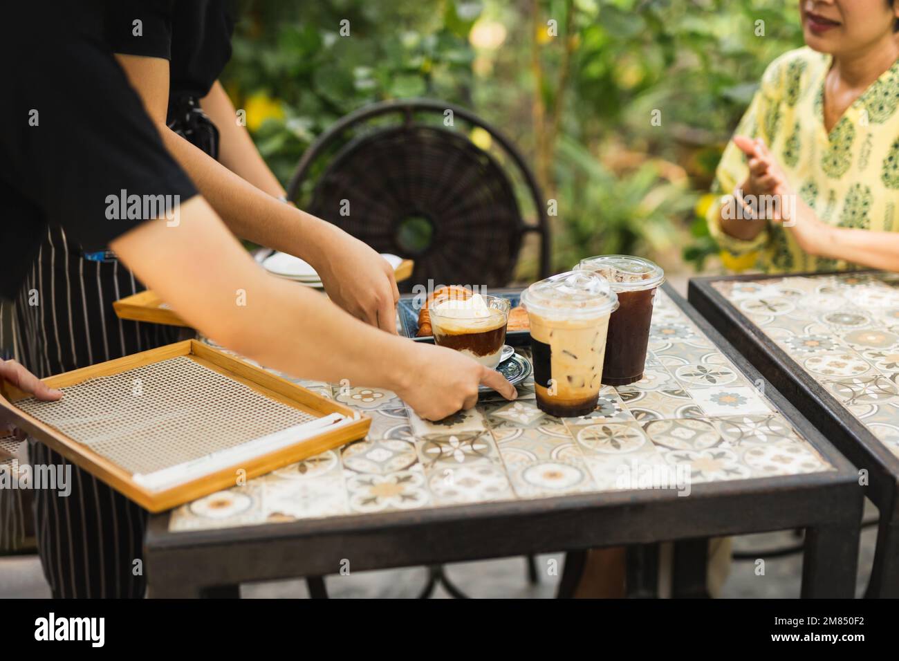 Livraison de boissons glacées par un serveur au client dans un café à l'extérieur. Banque D'Images