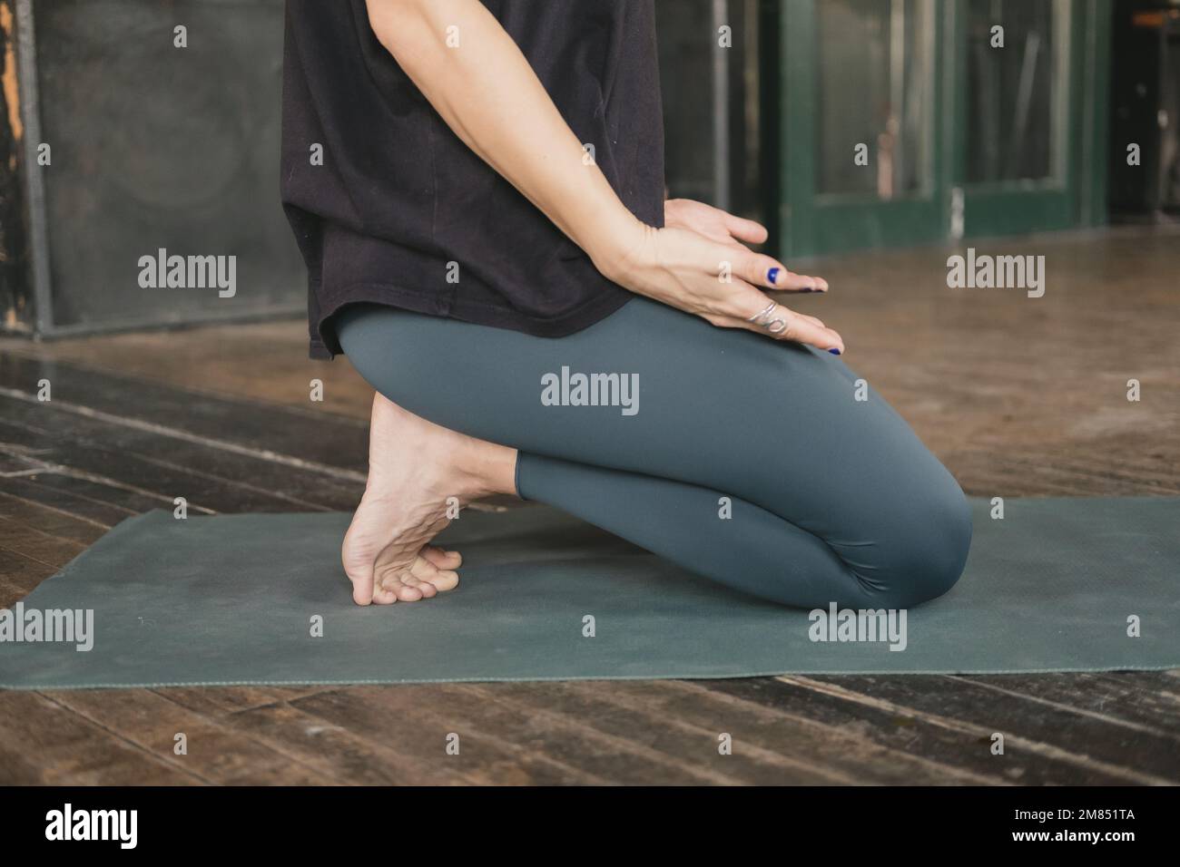 Femme non reconnaissable yogi nouveau professeur faisant une posture agenouillée avec les orteils repliés mains reposant sur les jambes avec les paumes vers le haut, entraînement de yoga, pieds nus Banque D'Images