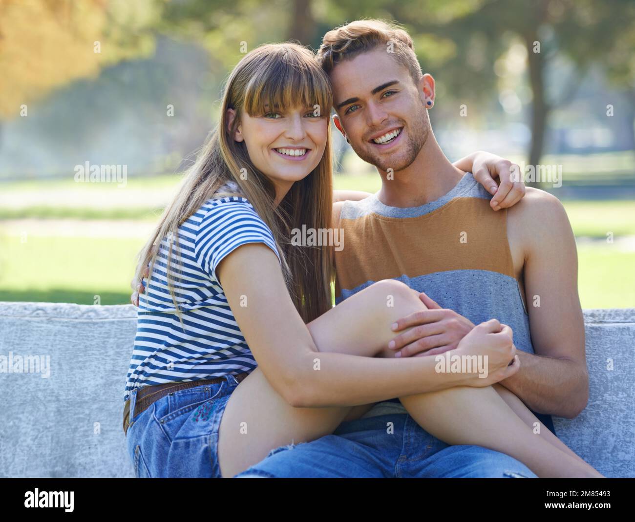 Heureux d'être ensemble. Portrait d'un jeune couple heureux assis sur un banc de parc. Banque D'Images