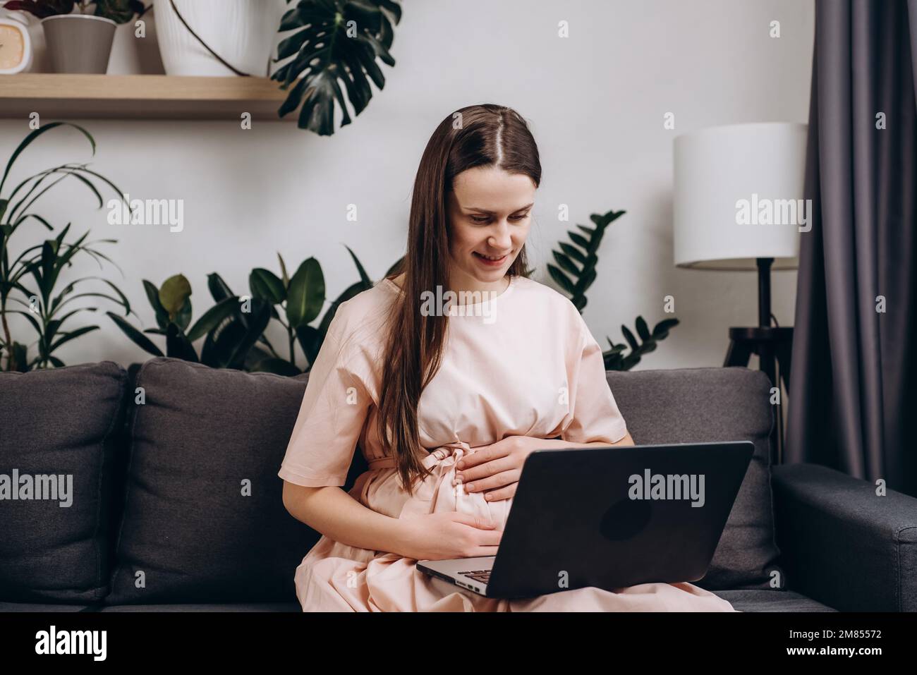 Heureuse belle femme enceinte assise sur un canapé confortable à l'aide d'un ordinateur portable ayant conversation d'appel vidéo à la famille, parler à obstétricien-gynécologue, recevoir Banque D'Images