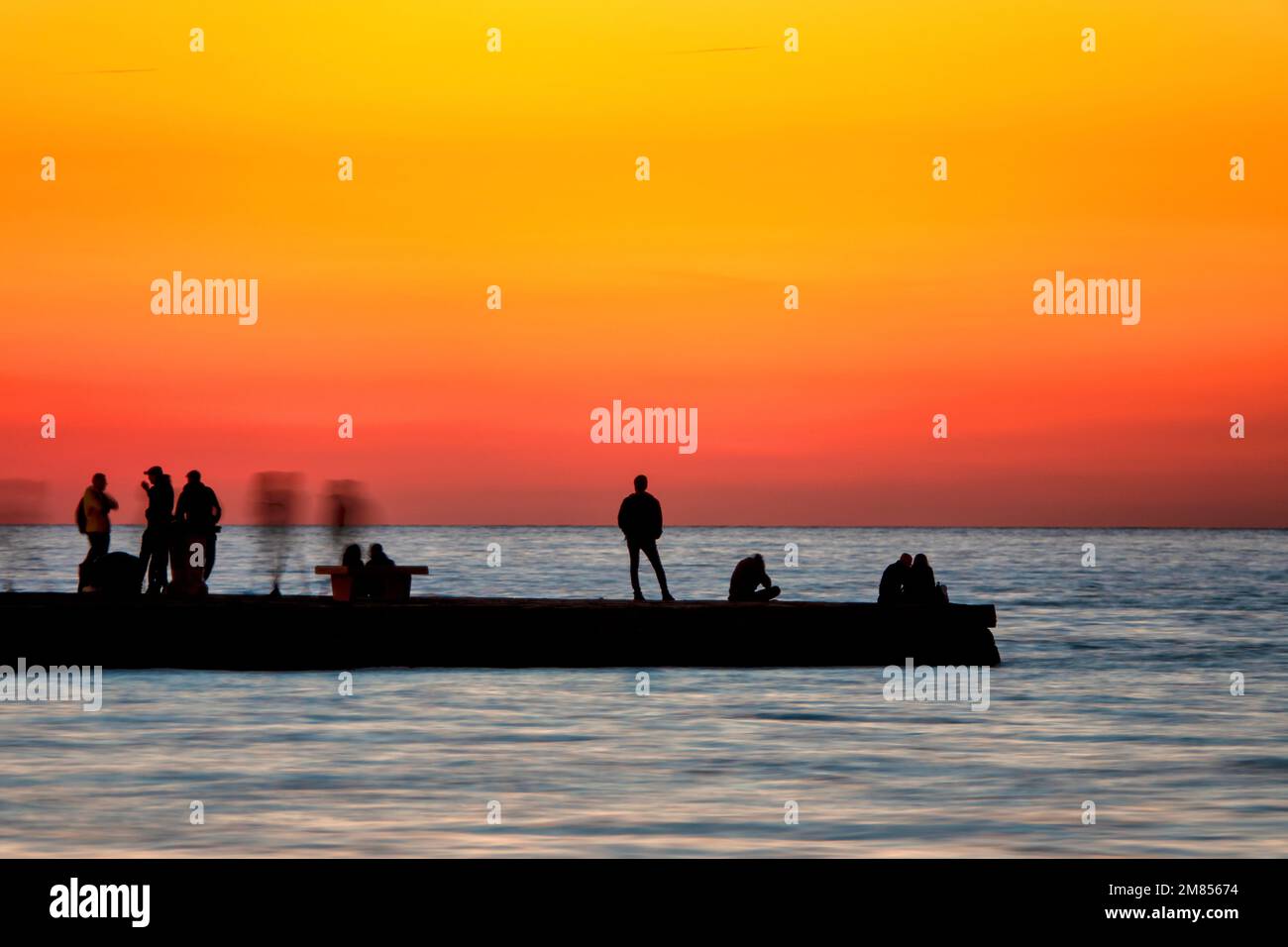 Silhouette de gens regardant le coucher du soleil sur le Molo Audace dans le vieux port de Trieste, Italie Banque D'Images