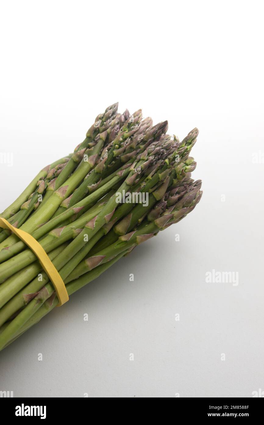 Image d'un bouquet d'asperges vertes nouées avec un élastique sur un fond blanc neutre Banque D'Images