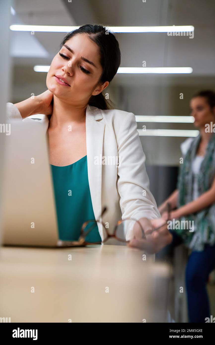 Jeune femme au bureau travaillant sur un ordinateur portable avec stress, douleur au cou et épuisement. Banque D'Images