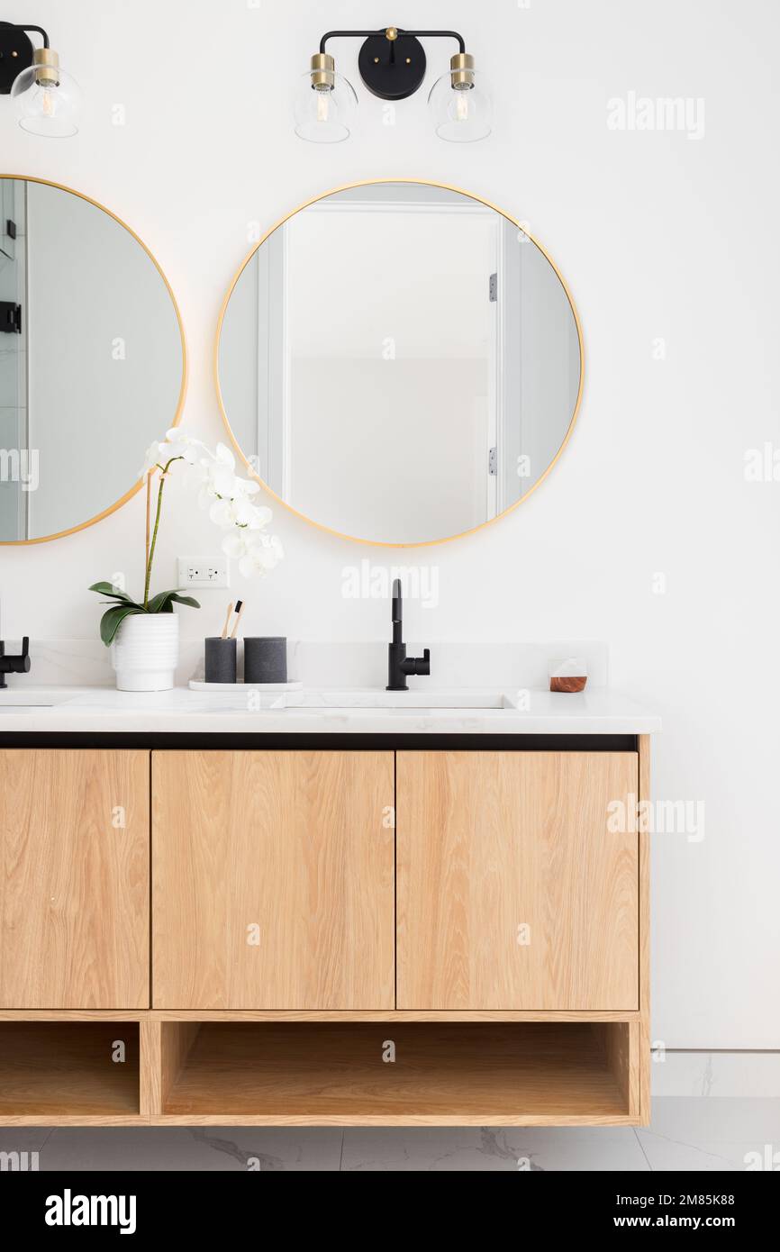 Une belle salle de bains avec un meuble en bois flottant, un comptoir en marbre et des miroirs circulaires dorés. Banque D'Images