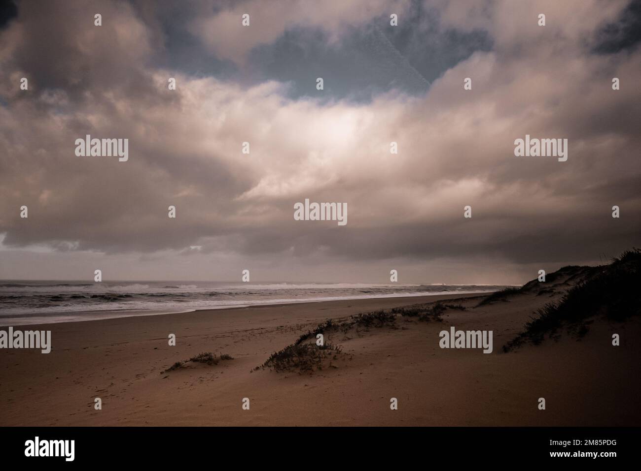 Un ciel spectaculaire avec des nuages orageux sur les dunes et l'océan Atlantique dans une plage sauvage et vide. Tons sombres et couleurs désaturées. Plage de Quiaios Banque D'Images