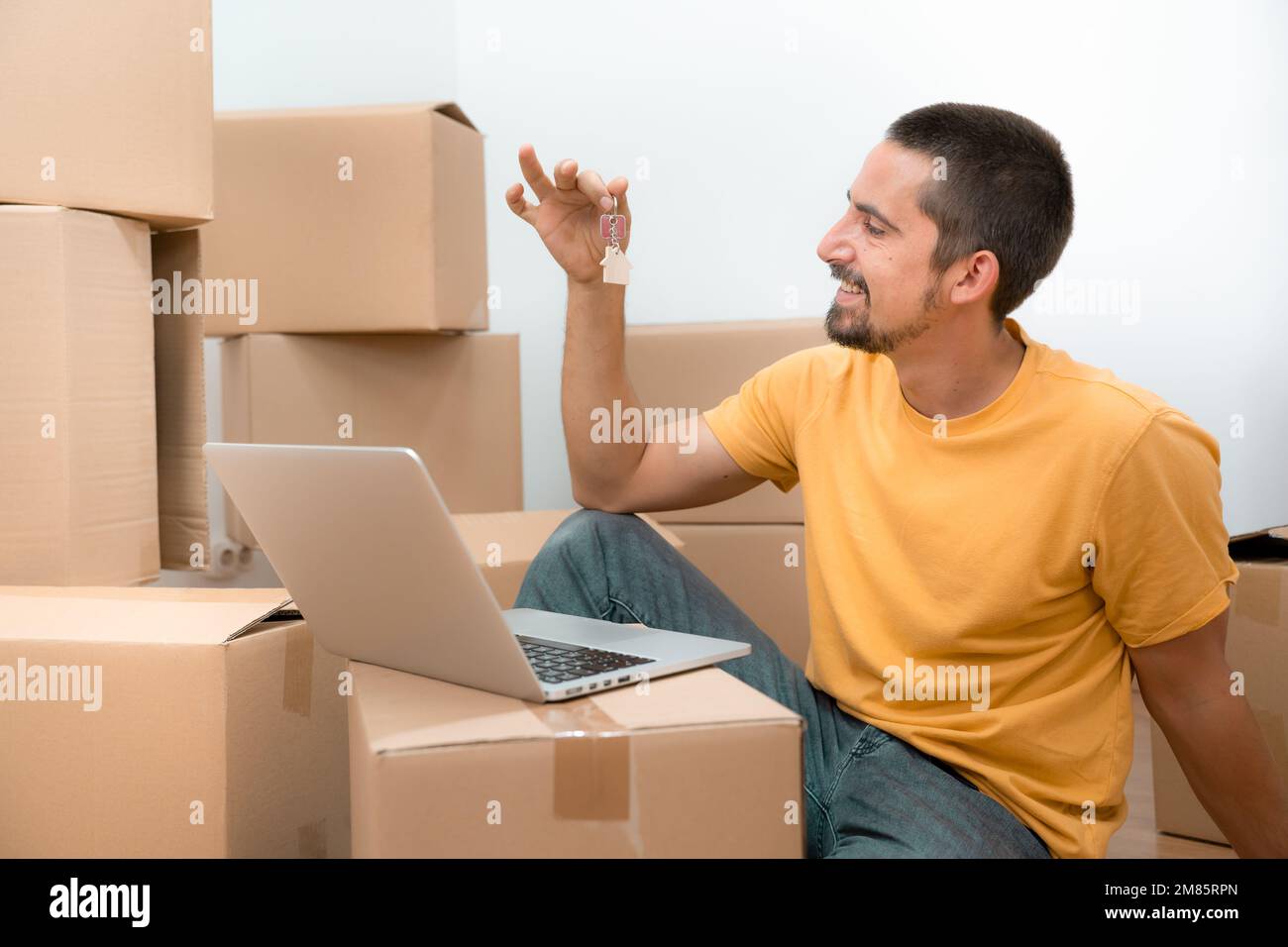 Heureux homme caucasien avec les clés de sa nouvelle maison appartement et ordinateur portable entre les boîtes. Banque D'Images