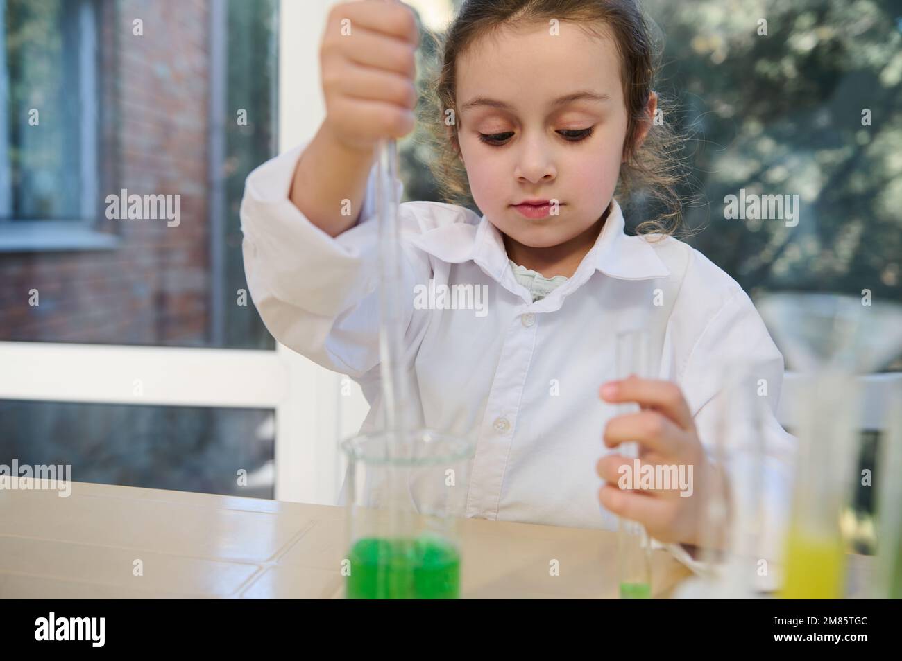Petite fille d'école utilisant une pipette graduée et un tube à essai, conduit des expériences chimiques, dans le laboratoire de chimie scolaire Banque D'Images
