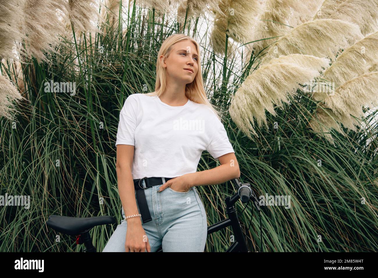 Jeune belle fille pose dans un t-shirt blanc à côté de son vélo. Maquette horizontale. Banque D'Images