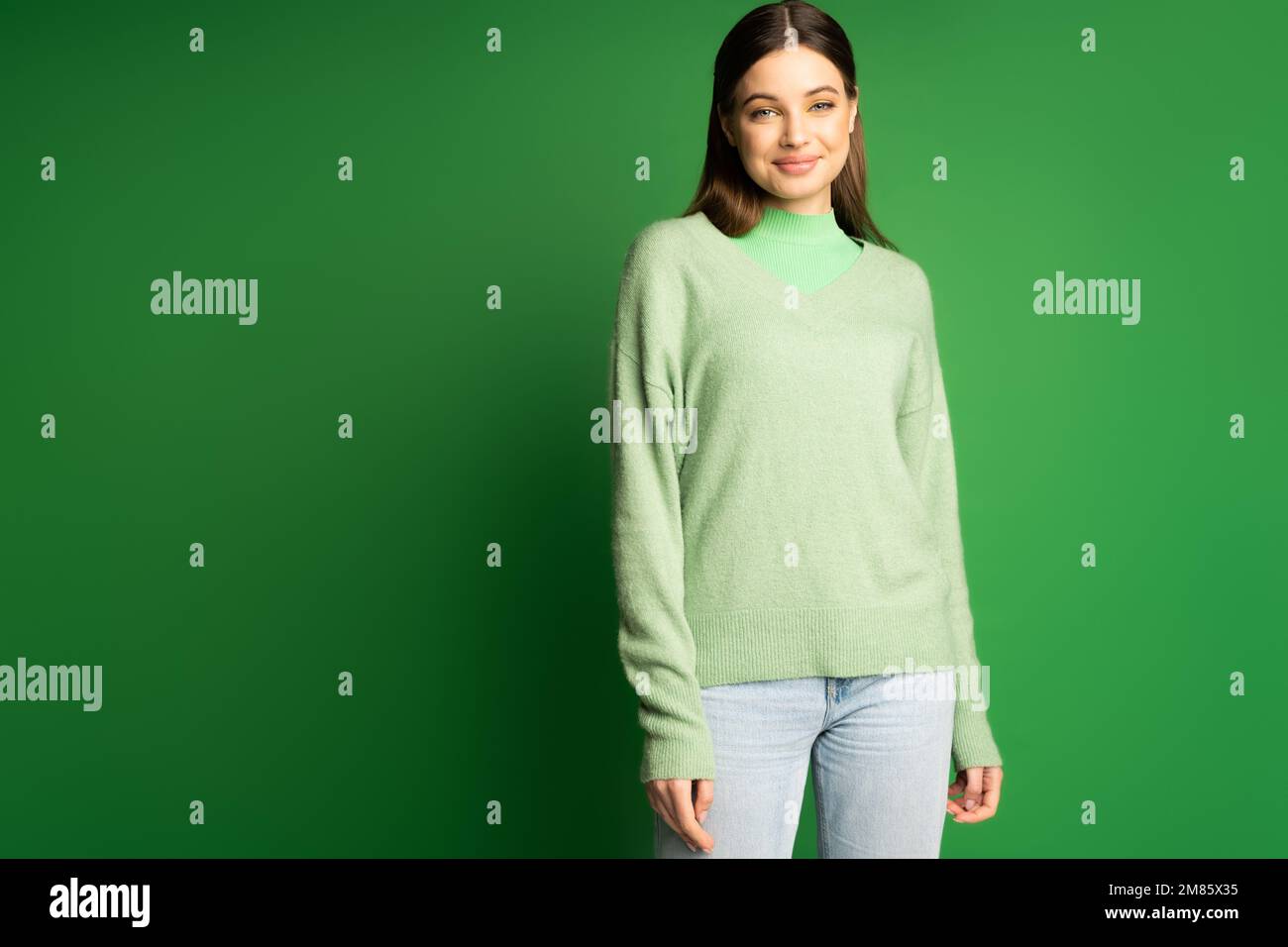 Fille positive de l'adolescence en pull et jeans debout sur fond vert Banque D'Images