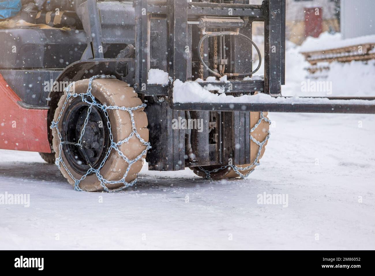 Roue du tracteur avec chaîne. Tracteur ou chargeur sur une route enneigée glissante. Les chargeurs se conduisent sur la neige avec des chaînes antidérapantes. Banque D'Images