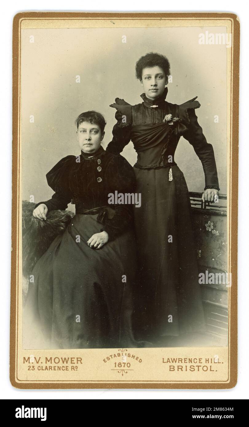 Original CDV (carte de visite ou carte de visite) d'une jeune femme victorienne riche / classe moyenne mixte / multi ethnique avec sa mère. Peut-être qu'ils sont en deuil car la mère semble très triste et porte du noir. Femme victorienne. La robe de jeune femme a des manches ailées typiques de 1897 ou 1898 et la mère porte des manches bouffantes qui commençaient à réduire en taille à partir de la fin des années 1890 Du studio M. Mower, 23 Clarence Road, Lawrence Hill, Bristol, Angleterre, ROYAUME-UNI Banque D'Images