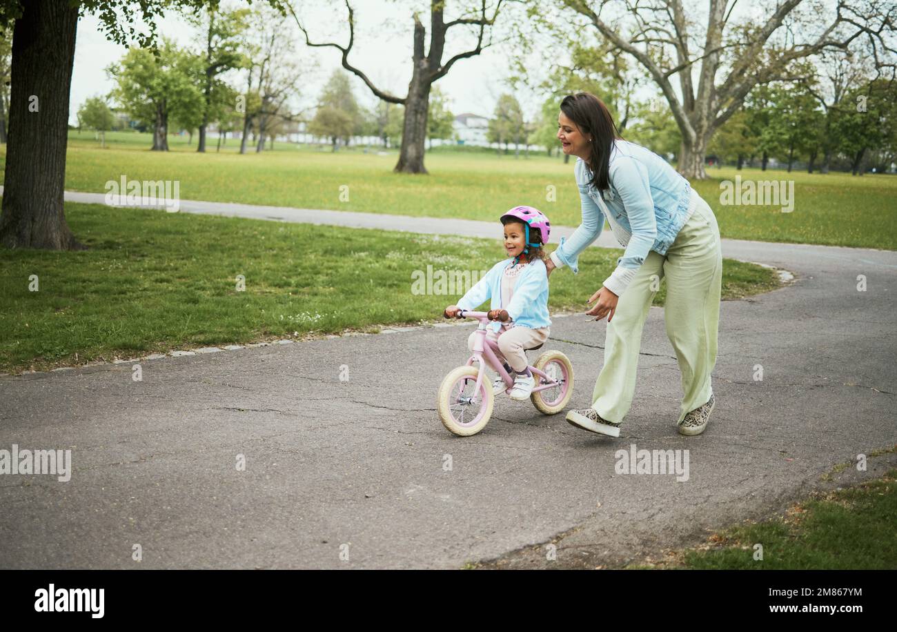 Enfants, vélo et une mère qui enseigne à sa fille comment faire du vélo dans un parc tout en se liant ensemble en famille. Nature, amour et enfants avec une fille Banque D'Images