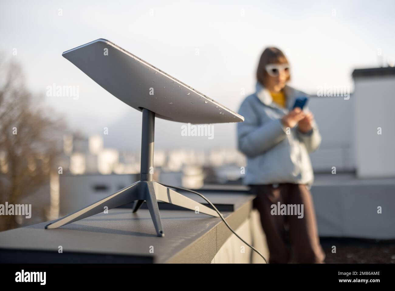Femme avec téléphone utilise Starlink satellite Internet sur le toit Banque D'Images