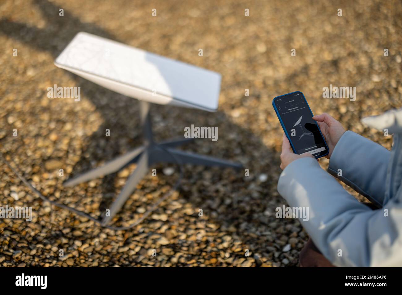 Téléphone avec application Starlink en cours d'exécution et antenne parabolique en arrière-plan Banque D'Images