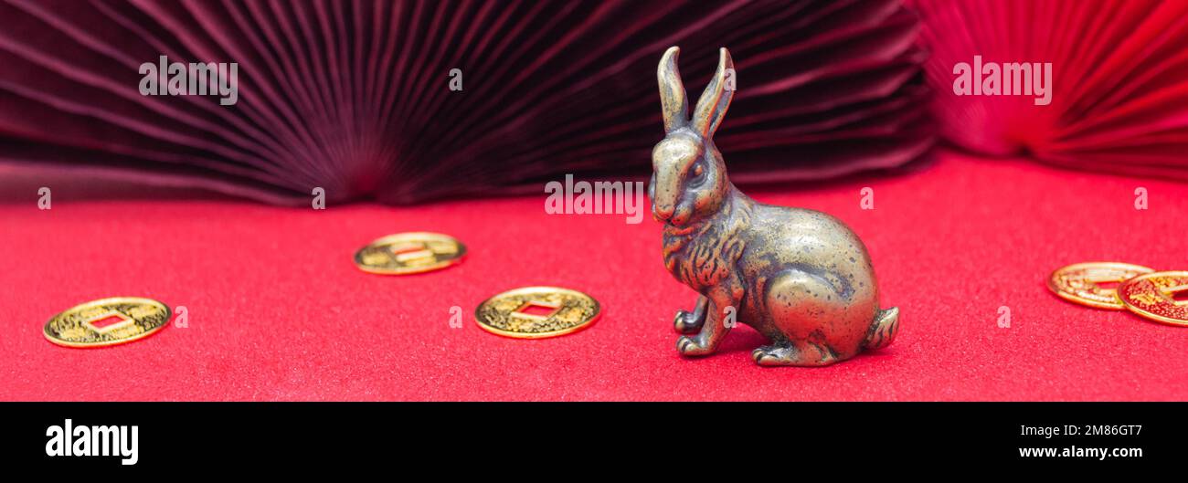 Bannière avec une figure en bronze d'un lapin avec des pièces en or - le symbole du nouvel an chinois 2023 sur fond rouge, espace copie. Banque D'Images