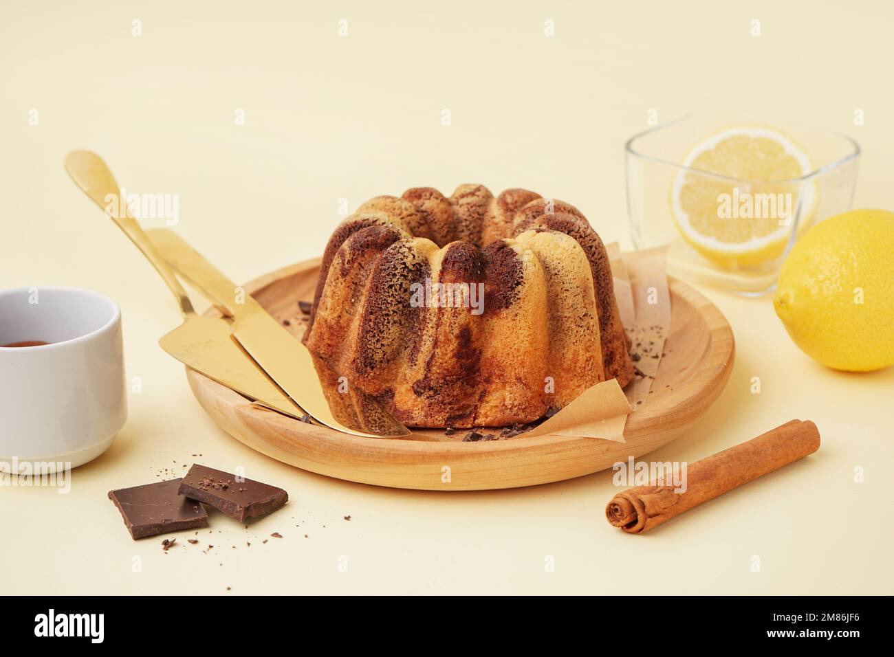 Assiette en bois avec délicieux gâteau, citrons et cannelle sur fond jaune Banque D'Images