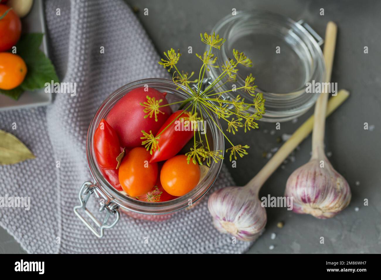 Conserver les tomates fraîches et marinées, les assaisonnements et l'ail sur une table en béton gris. Aliments fermentés sains. Légumes en conserve à la maison. Vue de dessus Banque D'Images
