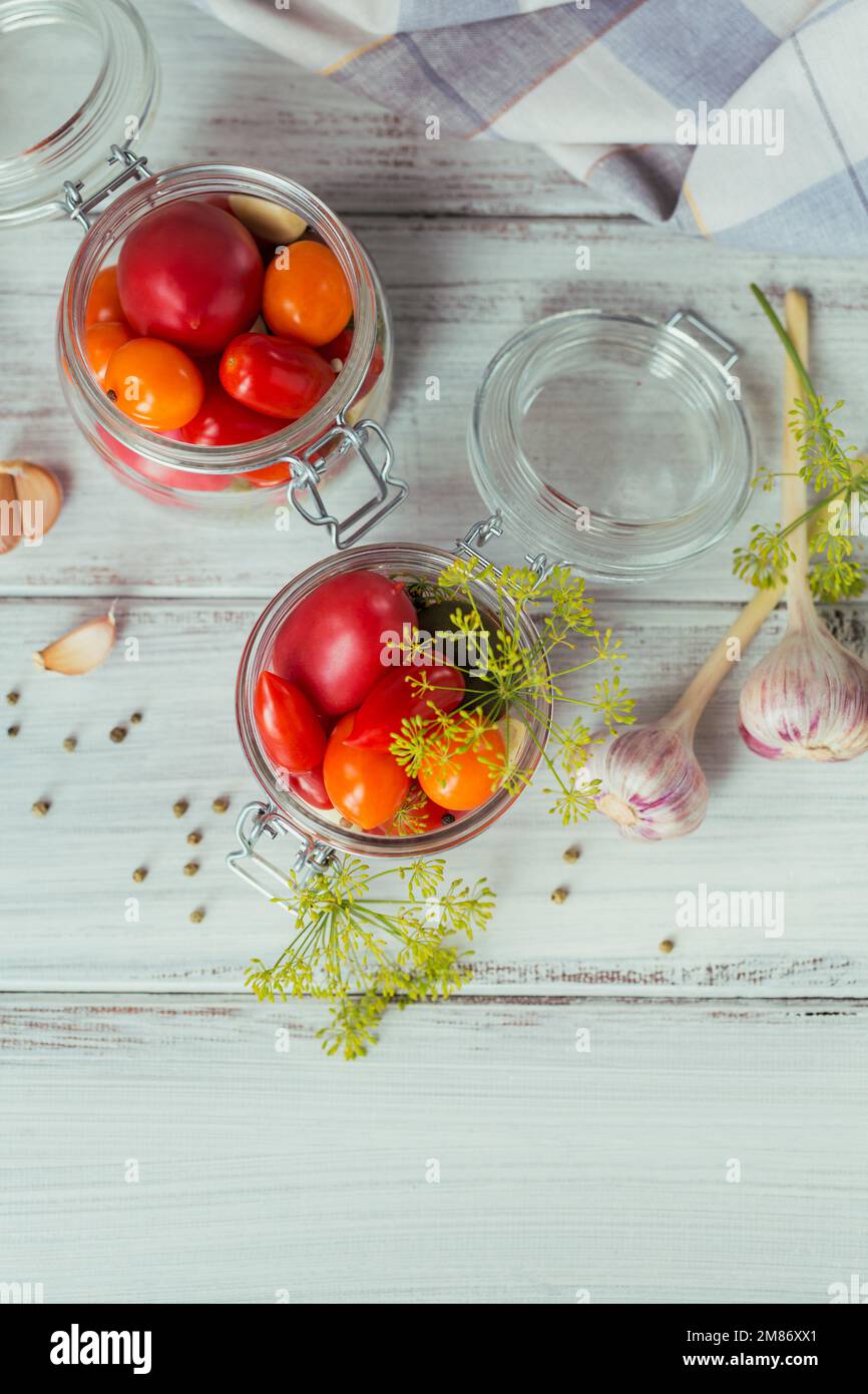 Conserver les tomates fraîches et marinées, les assaisonnements et l'ail sur une table en bois blanc. Aliments fermentés sains. Légumes en conserve à la maison. Vue de dessus Banque D'Images