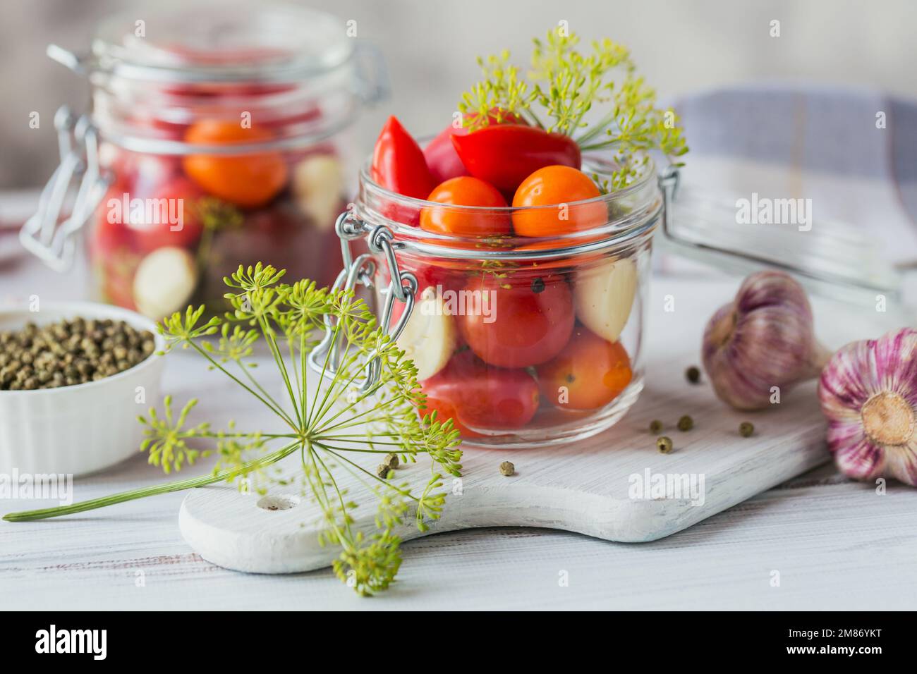 Conserver les tomates fraîches et marinées, les assaisonnements et l'ail sur une table en bois blanc. Aliments fermentés sains. Légumes en conserve à la maison. Banque D'Images