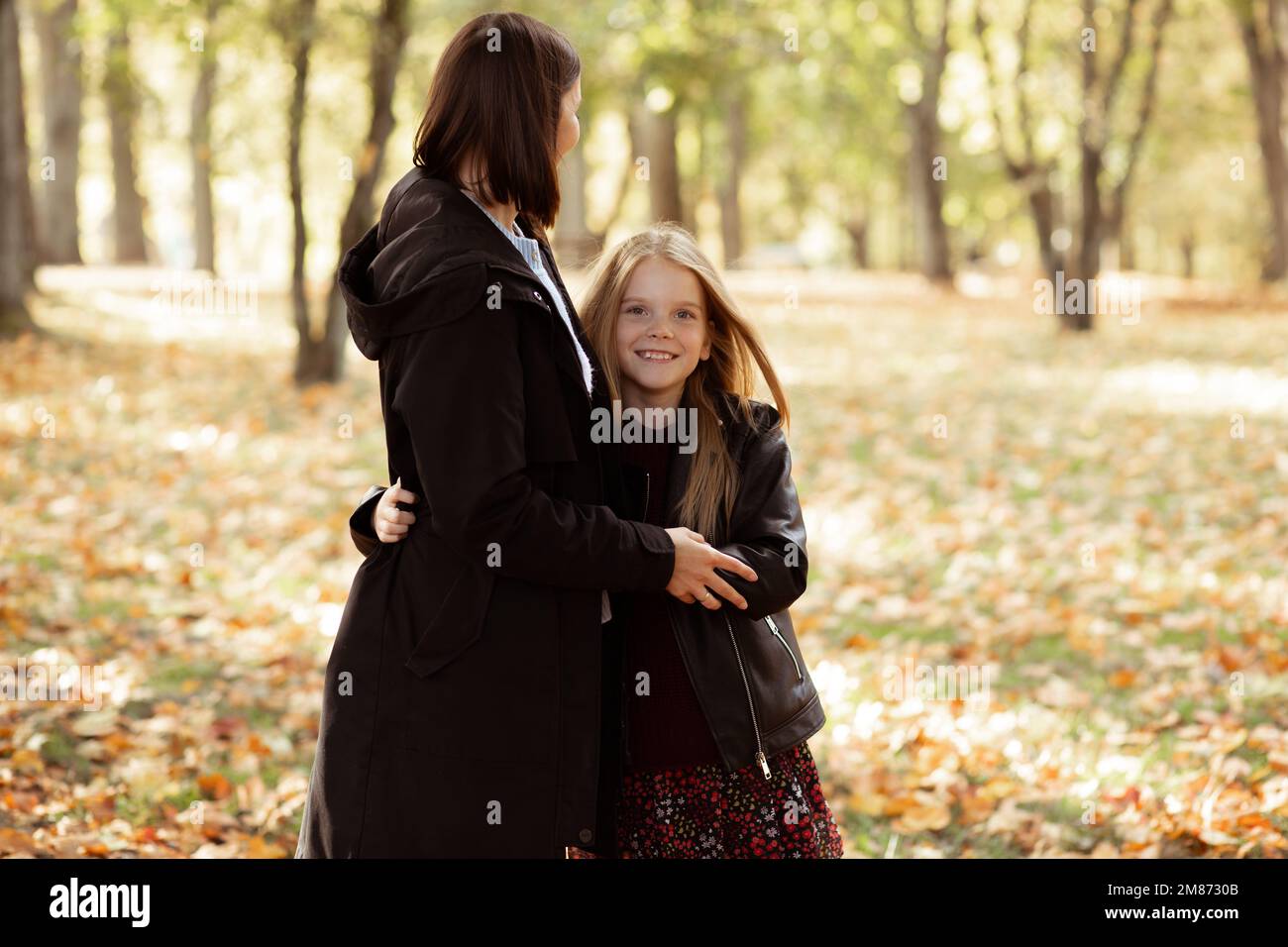 Charmante famille insouciante de la jeune mère et fille blonde dans la veste en cuir embrassant, regardez l'appareil photo dans la forêt d'automne Banque D'Images