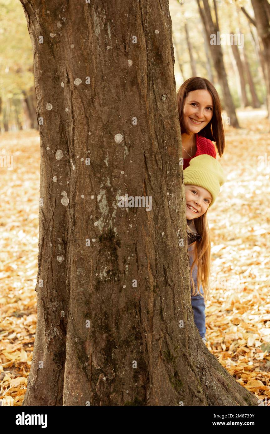 Vertical heureux, méfait mère et fille ont plaisir ensemble dans la forêt d'automne. Cachez derrière l'arbre, regardez l'appareil photo avec le sourire Banque D'Images