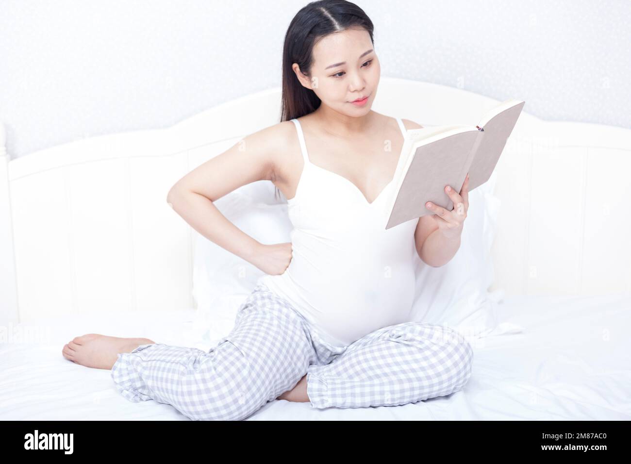 Les femmes enceintes se sont assises au lit pour lire un livre Banque D'Images